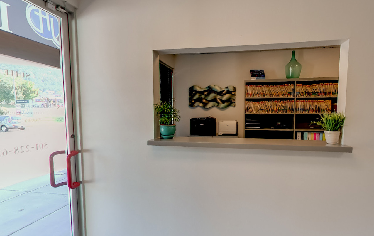 The image shows an interior space with a countertop displaying various items, including books and decorative objects, against a wall with a framed picture above it. A door with a red handle is visible on the left side of the frame.