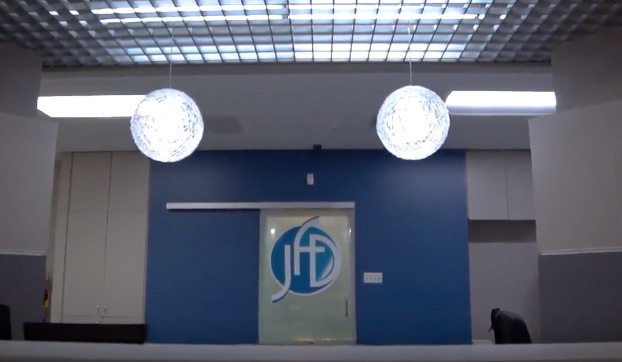 The image shows an interior office space with a modern design featuring a blue wall, white ceiling tiles, a desk with a lamp, and decorative spherical lights hanging from the ceiling.