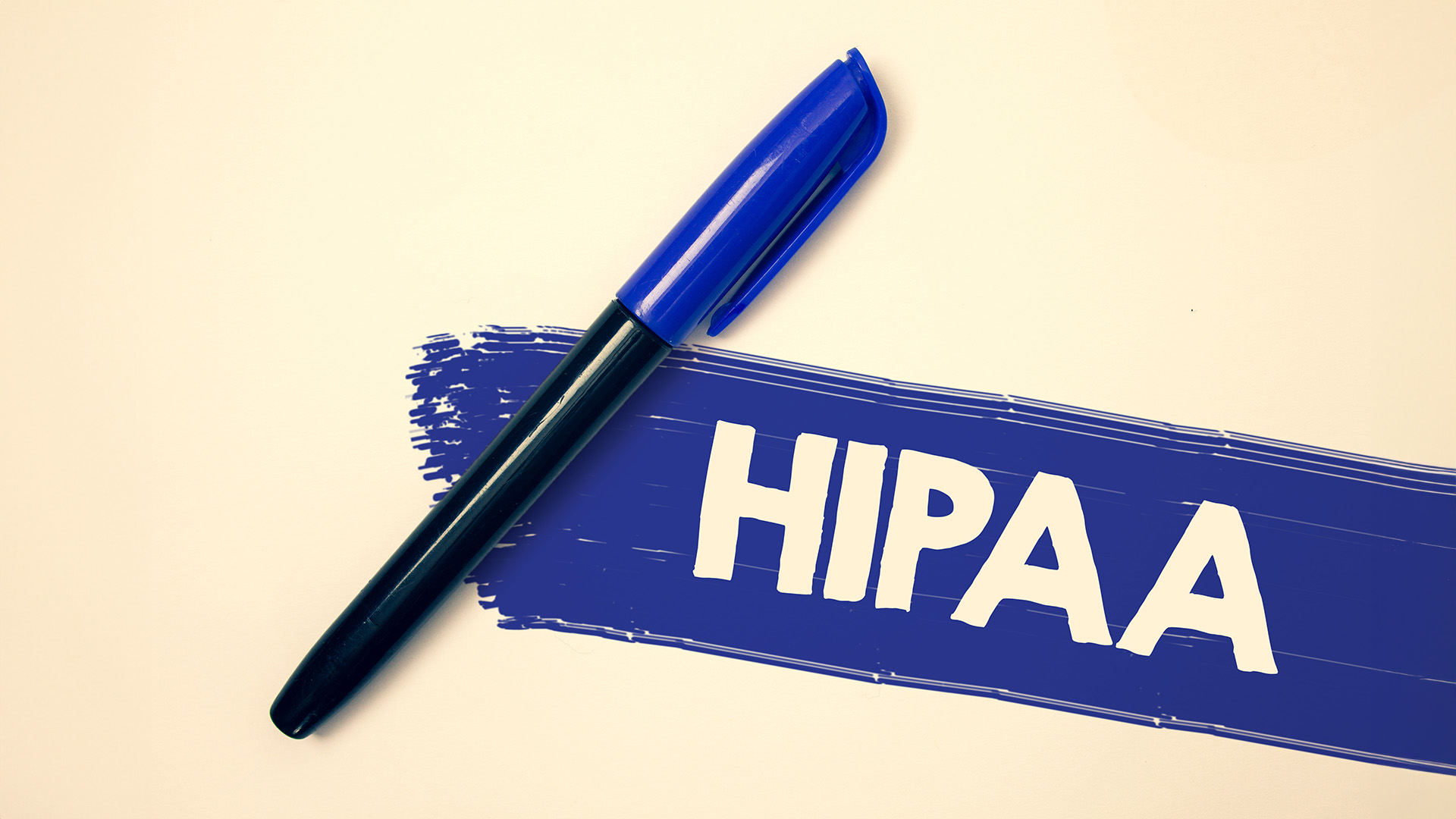 The image shows a blue marker pen resting on a white surface with a blue and white sticky note attached to it, which has the text  HIPAA  written on it in black ink.