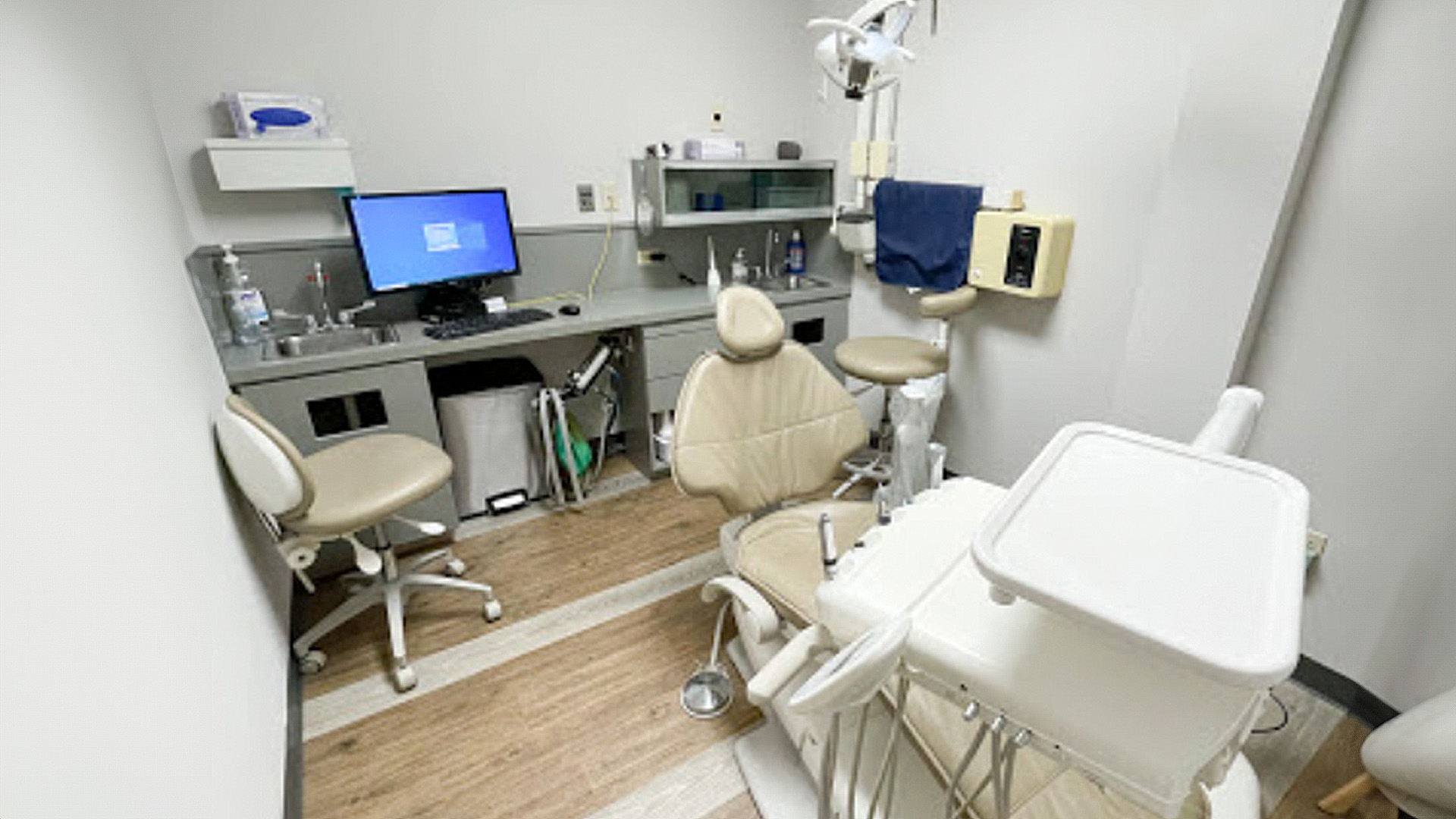 The image shows an interior view of a dental office with various dental chairs and equipment visible, including a computer monitor and a stethoscope.