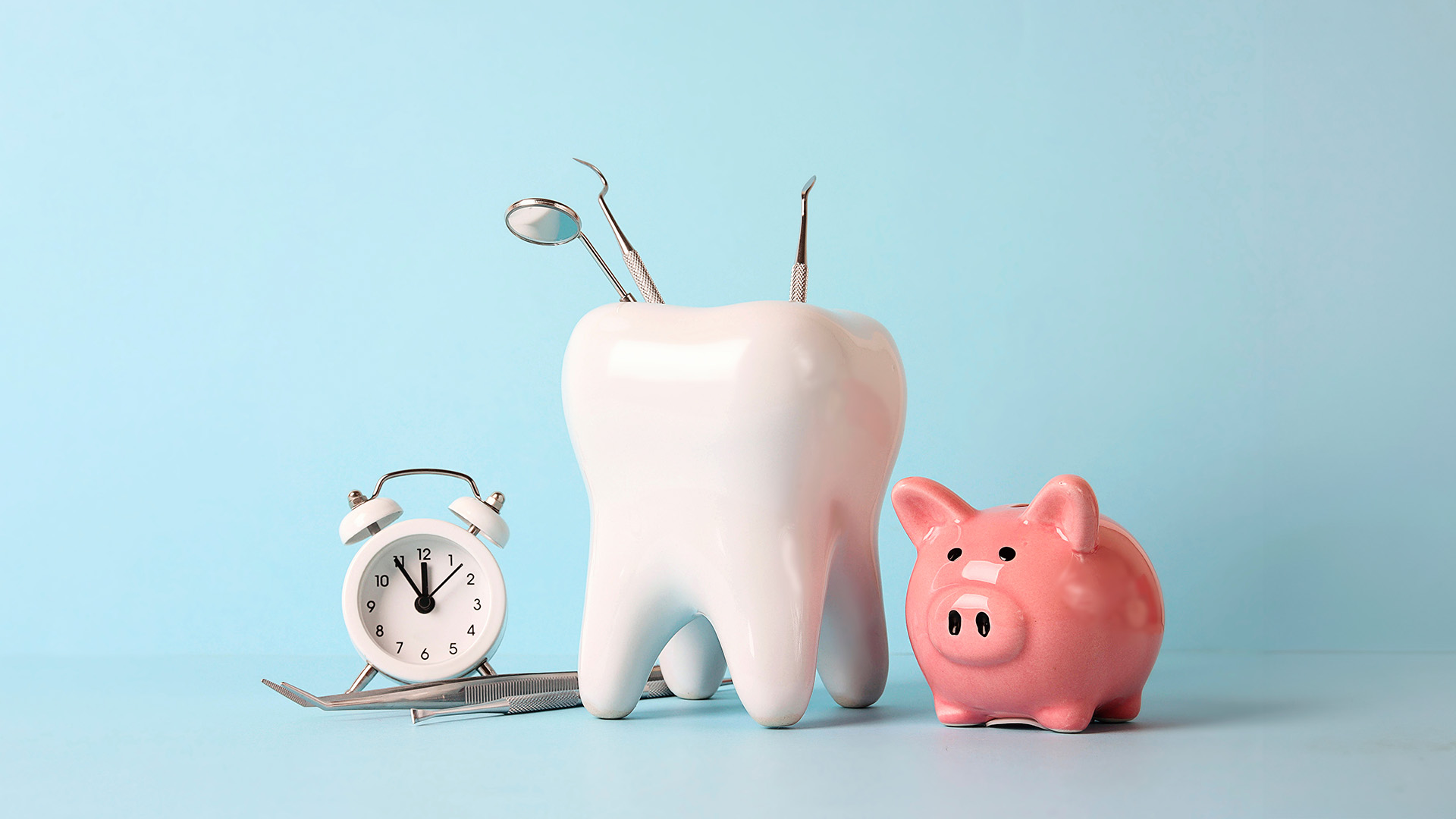 The image shows a toothbrush holder with two toothbrushes, a piggy bank, and a clock on a light blue surface with a white wall in the background.