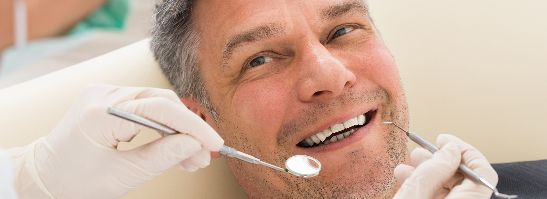 Man sitting in dentist s chair receiving dental treatment with smiling expression.