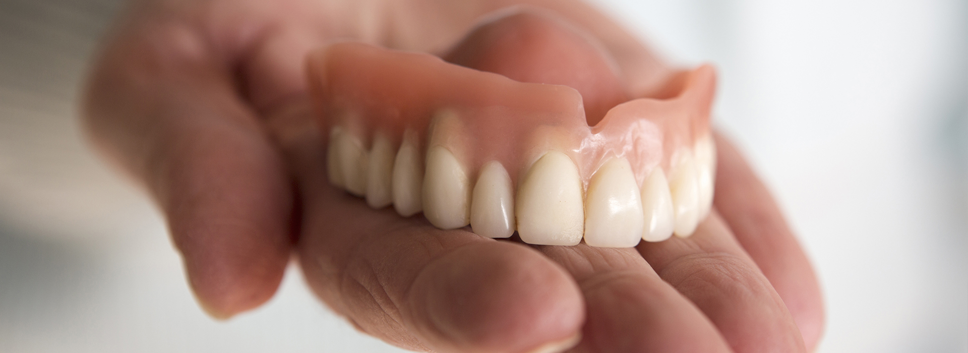 Hand holding a set of dentures with visible teeth.