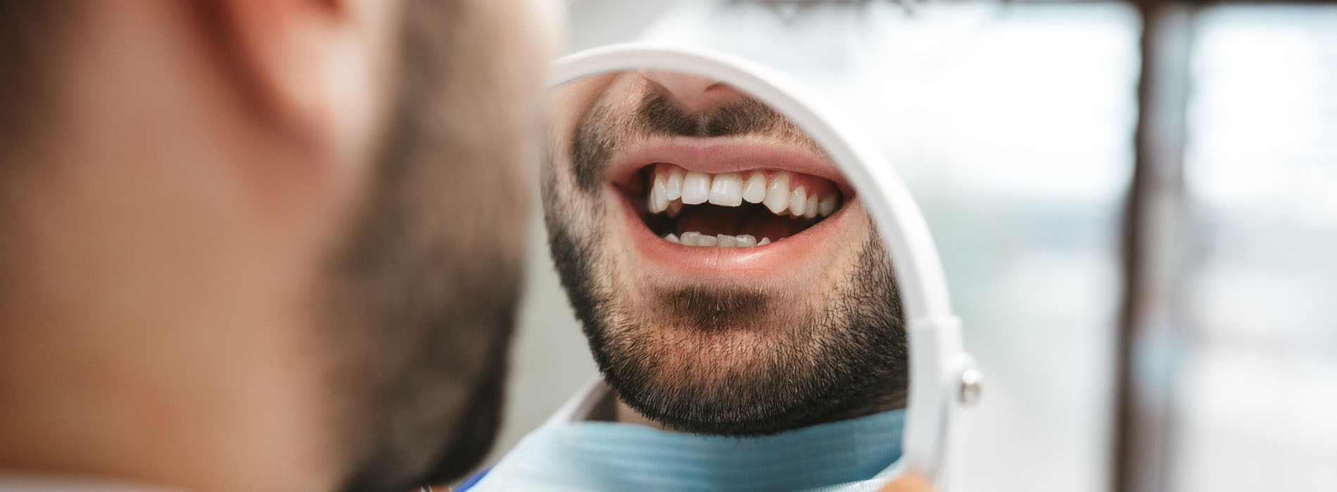 The image shows a man with a beard sitting in front of a dental professional, who appears to be examining his teeth, with both individuals smiling at the camera.