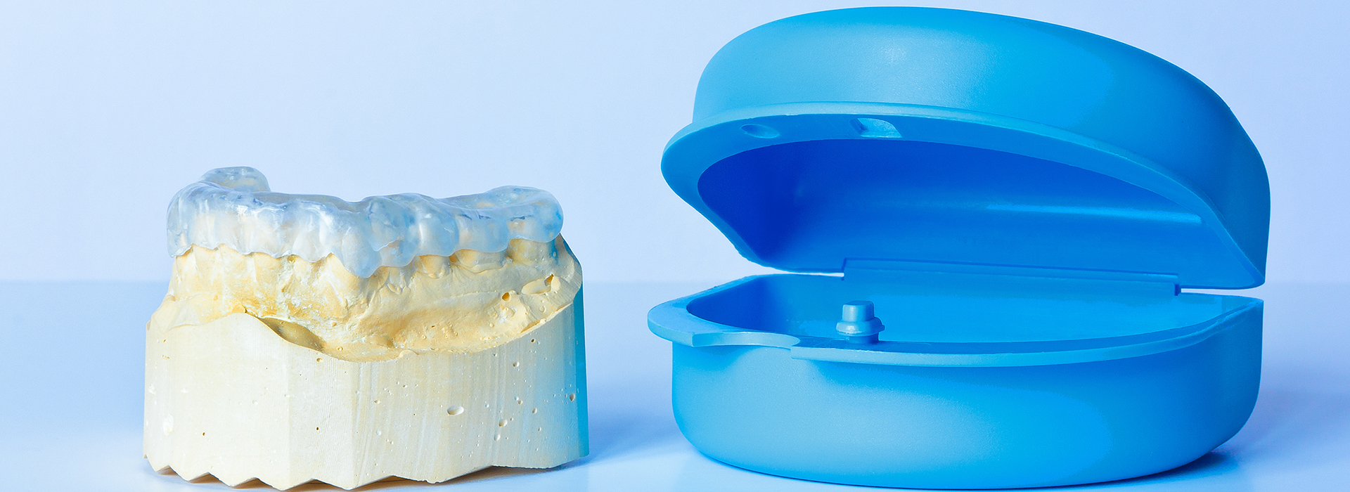 The image shows two objects  a transparent blue item with a smooth surface, which resembles a plastic container or mold, and a yellow object with a rougher texture that appears to be a dental implant or tooth replacement, placed next to each other for comparison or demonstration purposes.