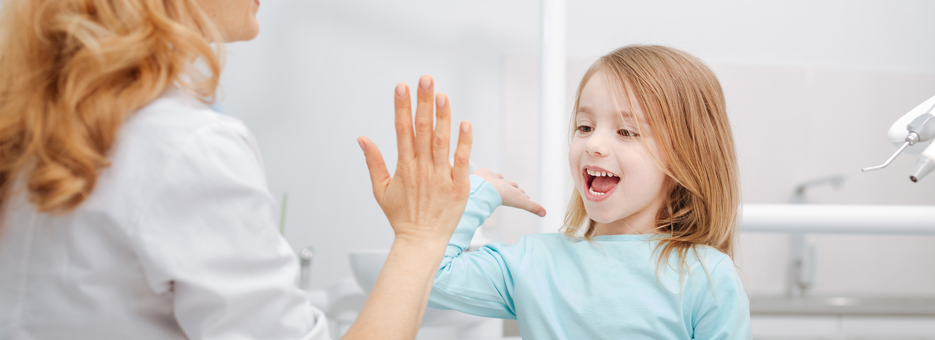 A woman and child interacting in a bathroom with a sink visible in the background.