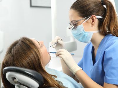 A dental hygienist performing a cleaning procedure on a patient s teeth while wearing full protective gear.