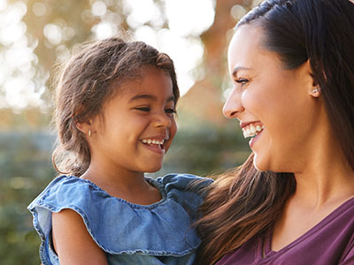 The image shows a woman and a young child smiling at each other with a blurred background, suggesting a close relationship between them.