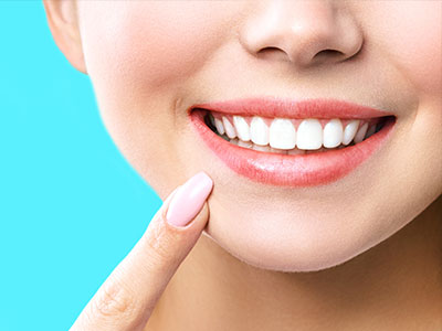 The image shows a close-up of a person s smiling face with a focus on their teeth and lips, set against a light blue background.